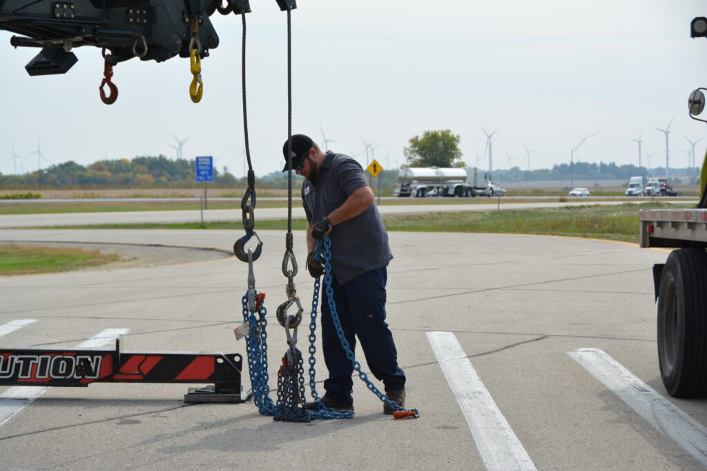 Tony's employee expertly handling and attaching chains, ensuring secure loading for towing services in Northern Iowa.