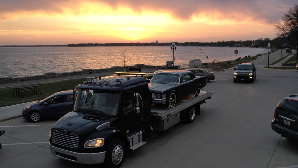 A classic or specialty car loaded on a Tony's flatbed truck, set against a breathtaking sunset backdrop in Northern Iowa.